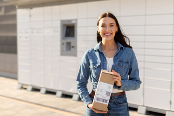 Happy lady holding mailbox in her hands, standing near automatic post terminal and smiling at...