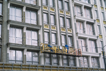 Workers in a construction cradle at a height perform installation work on the facade of the...