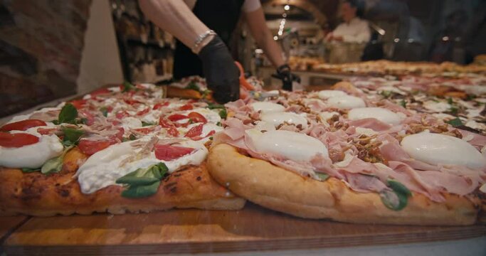 Street food in Italy pizzaiola cuts pizza with scissors. Delicious freshly baked cheese and ham pizza in a tourist pizzeria. High quality 4k footage