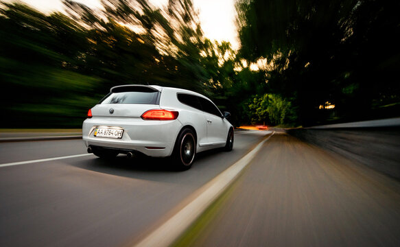 white Volkswagen Scirocco driving on a winding road at dusk. Low angle rear three quarter motion shot of VW hatchback with blurred background. Kyiv region, Ukraine - July 06 2014.