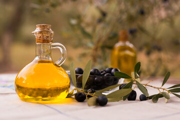 Olive oil in a glass bottle and green olives on the background of olive branches in the garden