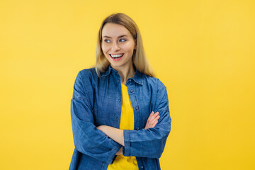young woman with pleasant smile and crossed arms isolated on yellow wall with copy space. Beautiful...