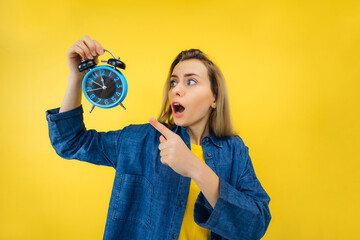 pretty young woman holding alarm clock pointing and shouting over yellow background. Late for work
