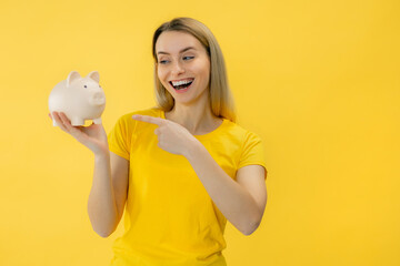 young woman point finger at pig coin bank, money box, for saving, deposit. Yellow background.