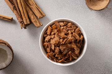 Coconut chips with cinnamon powder in bowl on gray background. Tasty sugar free snack. View from above.