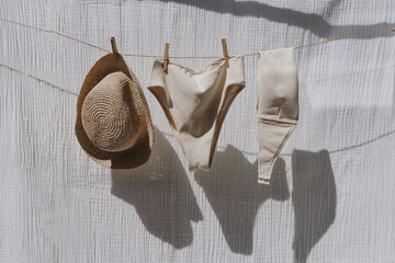 Female swimwear and straw hat hanging over white cotton cloth with strong shadows. Sunbathing on a...
