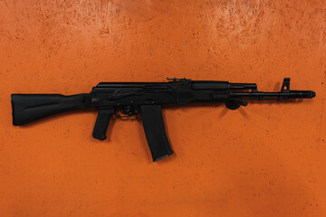 AK74m rifle on an orange wall in a shooting range.