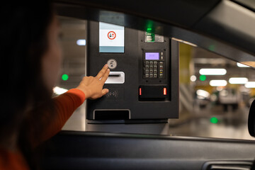 Young woman pressing button and waiting for the ticket at the parking meter at underground parking...