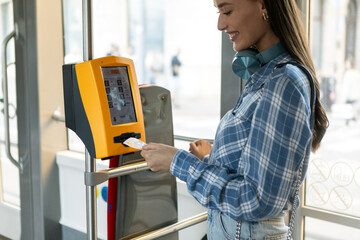 Woman passenger taking ticket in public transport in the tram, using vending tickets machine inside...