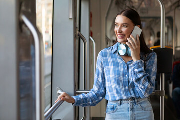 Cheerful young lady talking on cellphone while taking public city bus, female passenger looking out...