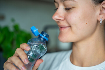 Young woman drinking from a bottle with stationary plastic cap. The new design means the cap...