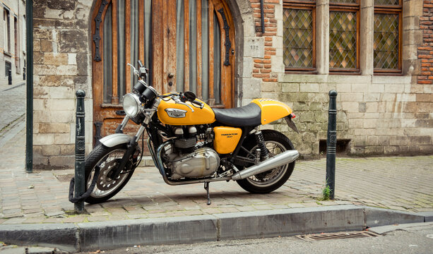 Triumph Thruxton 900 parked on the sidewalk. Yellow classic style motorcycle on the street in central Brussels near 16th century Bruegel House. Brussels, Belgium - October 09 2014.