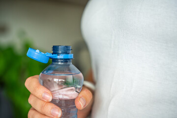 Bottle with stationary plastic cap in woman hand. The new design means the cap remains attached to the bottle after opening, making the entire package easier to collect and recycle