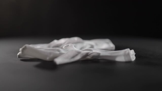 White gloves dropping on black surface close-up 4K