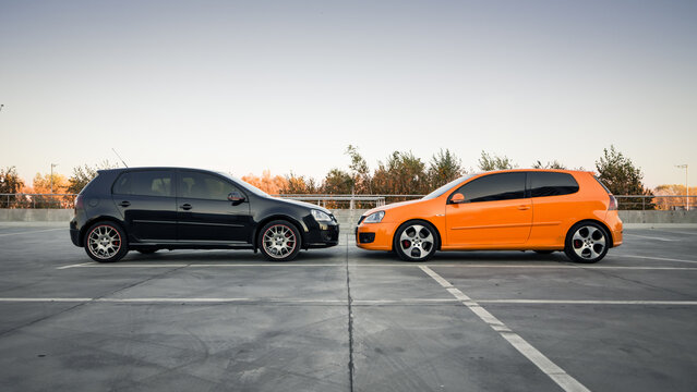 Side of black and orange Golf GTi parked on big empty parking lot. Side view of two Volkswagen hatchbacks. Kyiv region, Ukraine - October 14 2014.