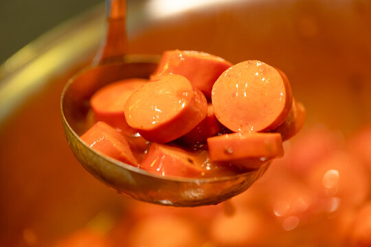 Salsicha cortada em rodelas com molho de tomate em uma concha de metal em foto com vis&atilde;o de perto.