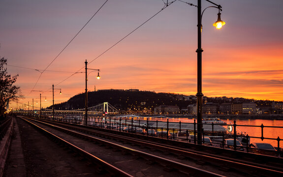 Glowing orange sunset in Pest. View from Jane Haining rakpart street at the montaneous rigth bank of Danube (Buda). Tram line at the top of the embankment. Budapest, Hungary - December 20 2014.