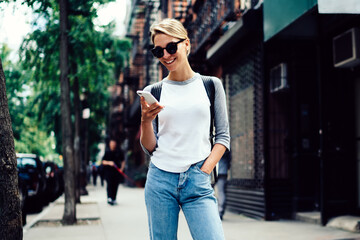 Portrait of cheerful hipster girl in casual outfit enjoying free time using mobile phone on...