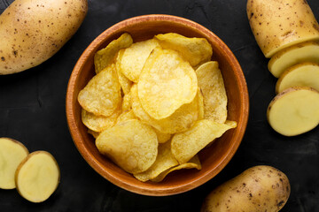 Potato chips in a wooden plate and raw potatoes background. Top view