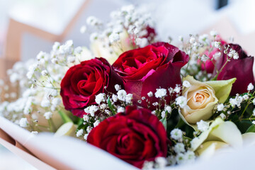 Bouquet of red and yellow roses with white flowers. The roses are arranged in such a way that they all face the same direction. Festive bouquet close-up.