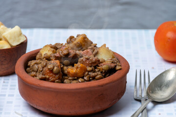 Close-up of a bowl of lentil stew biscuits, cutlery and tomato around.