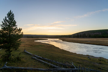 The Firehole River flows through Yellowstone National Park in Wyoming at sunset and golden hour on a fall evening.