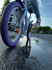 Naklejka premium Child rides a bicycle on a wet road, splashing through puddles during daytime
