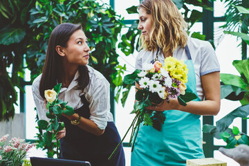Female colleagues working as florist in botanic orangery cooperating during creating floral...