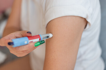 Woman injects herself with the drug Ozempic anti-diabetes pen into her arm at home. Weight loss and decreased blood sugar, concept idea.  injector dosing pen for subcutaneous injection