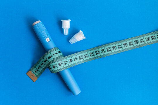modern drug pen injection Ozempic for weight loss with body measuring tape and needles on a blue background. drug for reducing sugar and diabetics.