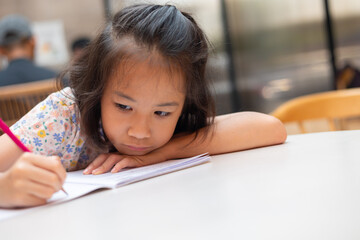 Face and eyes close up of adorable Asian kid girl who is writing with determination and...