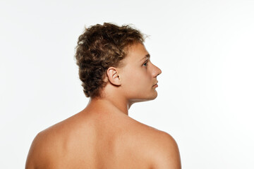 Rear view photo of young man with curly hair posing shirtless and looking away against white...