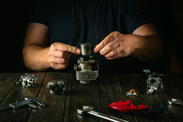 A mechanic is repairing a trimmer motor on a workbench in a workshop. Replacing the engine cylinder...