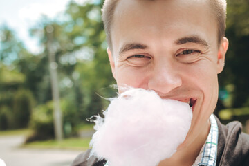 Man eats cotton candy in the park. Close-up portrait of a young 20 year Europeans eating a candy...