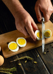 Preparing a dish of boiled eggs on the kitchen table. A knife in the hands of a cook for slicing...