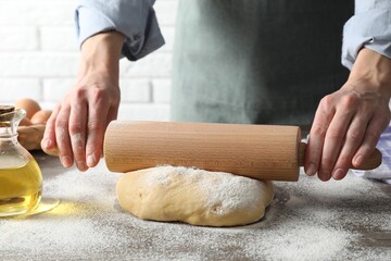 Woman rolling raw dough at table, closeup