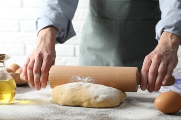 Woman rolling raw dough at table, closeup