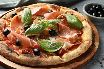 Tasty pizza with cured ham, olives, sun-dried tomato and basil on gray table, closeup