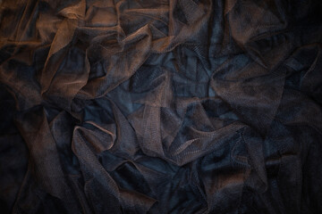 Black translucent fabric is draped and textured with numerous folds and creases, highlighted by soft, dim lighting.
