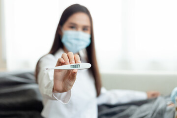 A woman wearing a white lab coat holding a thermometer. She is wearing a blue mask