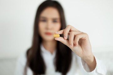 A woman is holding a yellow pill in her hand. She looks unhappy and is not smiling. The pill is...