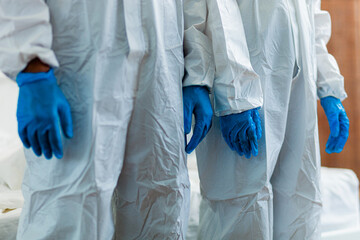 Three people in white protective clothing with blue gloves. The gloves are on their hands. The...