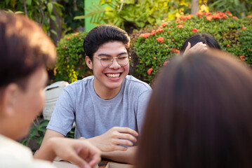 A young asian man in his late teens or early 20s enjoys the company of his friends, having a lively group conversation outside in a garden.