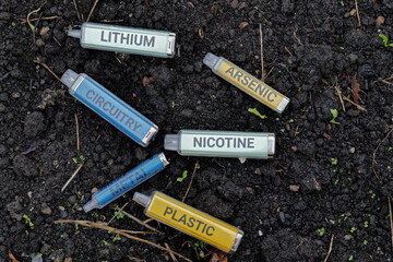 Disposable single use electronic cigarette vapes on dark wet soil with the words metal, nicotine,...