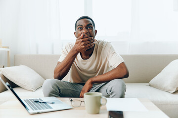 A tired African American freelancer working on a laptop, feeling sad and unhappy during a crisis,...