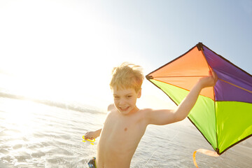 Boy, ocean and kite on beach with fun, adventure and playing in sunshine for summer holiday....