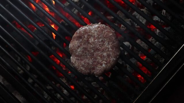 Top view of a flipping a beef-burger with a stainless spatula on a charcoal grill