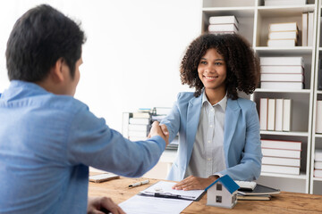 A real estate agent and a customer discuss a contract to buy insurance or a loan on real estate or property. A real estate agent shakes hands and delivers a sample home to the customer.