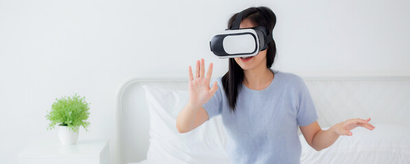 Young asian woman wearing vr headset playing game with excited on bed in the bedroom at home,...