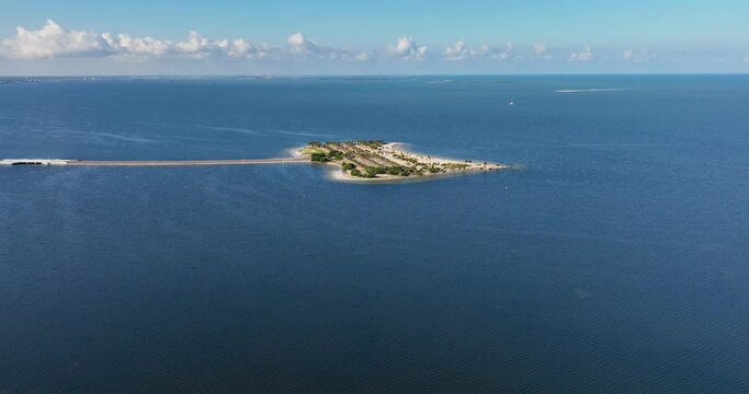 Aerial view of Fred Howard Park in Tarpon Springs, Florida, featuring parking lots, palm trees, sandy beaches, and surrounding blue waters under a clear sky.
